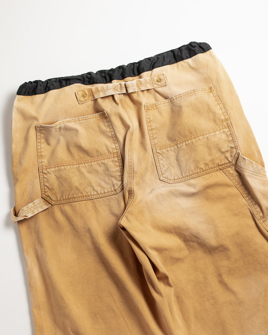 【 商品名：リメイクダブルニーダックペインターパンツ 】

本製品は、レングスをやや長めに設定したイエローカラーのペインターパンツです。ウエスト部分にはナイロンオックス生地で切り替えを施し、ワーク感を抑えたバランスの良いデザインに仕上げています。生地には頒布の中でも最も薄手の11号帆布生地を使用しており、強度・耐久性に優れるだけでなく、着用を重ねるごとにアタリなどの経年変化を味わえる素材です。また、水や薬品の使用量を抑えながら生地の凹凸部分のアタリを強調し、同時に自然な脱色感を与える特殊エイジング加工に加え、サンフェードによるダメージ加工も施すことで、より深みのある表情に仕上げています。