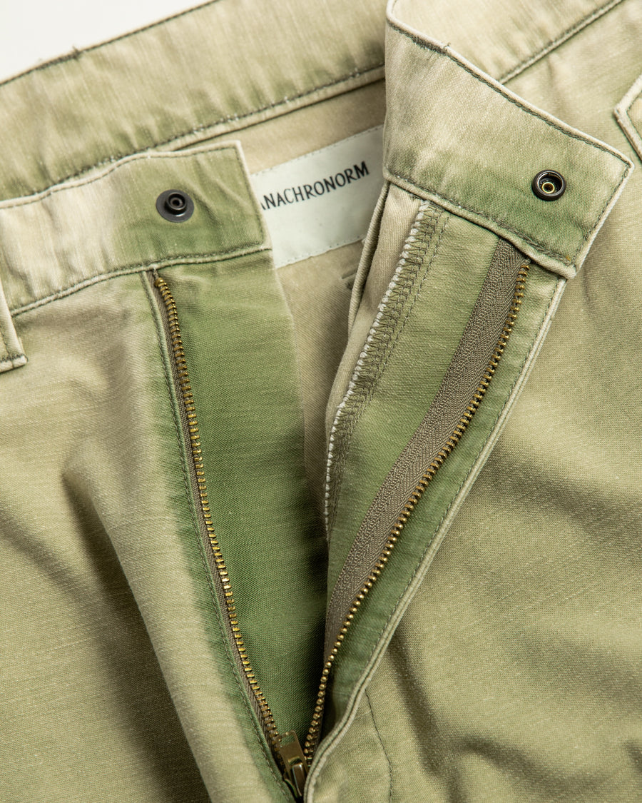 フラップポケットや膝のタック、裾のドローコードなど、ミリタリーのディテールをふんだんに取り入れた一本。内側に配置されることの多いポケットをあえて外側に設けたカーゴポケットが特徴です。ムラ糸で織り上げたバックサテン生地は、ハリとコシのある質感が魅力。さらに、水や薬品の使用を抑えながら生地の凹凸を際立たせる特殊エイジング加工を施し、深みのあるオリーブカラーに仕上げています。