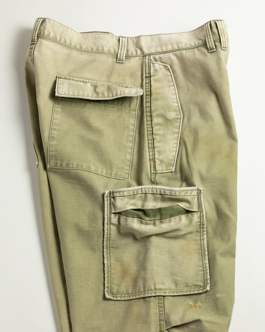 フラップポケットや膝のタック、裾のドローコードなど、ミリタリーのディテールをふんだんに取り入れた一本。内側に配置されることの多いポケットをあえて外側に設けたカーゴポケットが特徴です。ムラ糸で織り上げたバックサテン生地は、ハリとコシのある質感が魅力。さらに、水や薬品の使用を抑えながら生地の凹凸を際立たせる特殊エイジング加工を施し、深みのあるオリーブカラーに仕上げています。