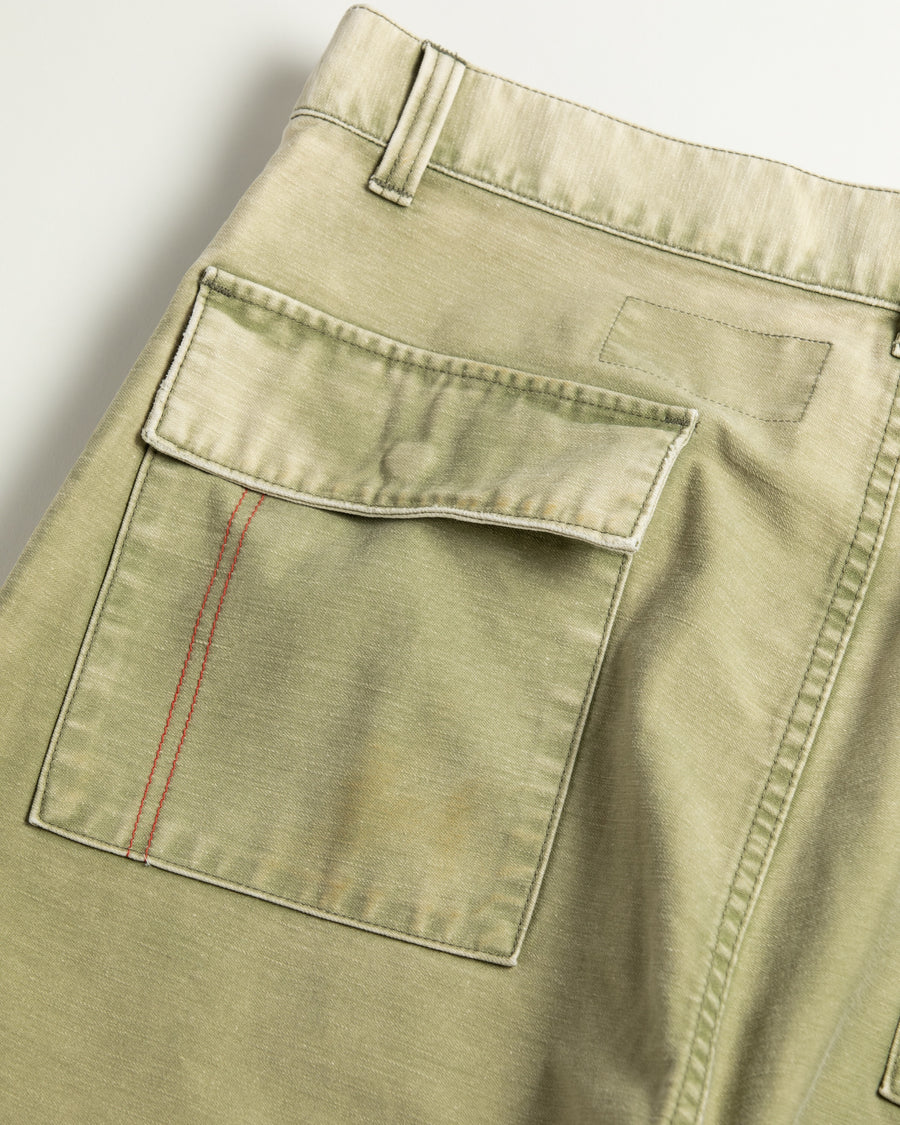 フラップポケットや膝のタック、裾のドローコードなど、ミリタリーのディテールをふんだんに取り入れた一本。内側に配置されることの多いポケットをあえて外側に設けたカーゴポケットが特徴です。ムラ糸で織り上げたバックサテン生地は、ハリとコシのある質感が魅力。さらに、水や薬品の使用を抑えながら生地の凹凸を際立たせる特殊エイジング加工を施し、深みのあるオリーブカラーに仕上げています。