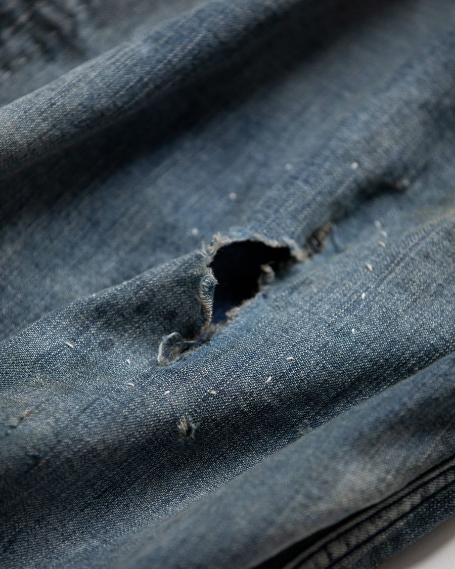 ライトオンスデニムを二重縫製で仕立てたフルジップパーカー。
経糸にジンバブエコットン100％、緯糸に綿麻混紡糸を用いたデニムは、シャープなムラ感と粗野な風合いでヴィンテージ感を演出。
全体にエイジングを施し、ハードダメージと手作業のステッチワークで仕上げたリメイク加工が特徴です。