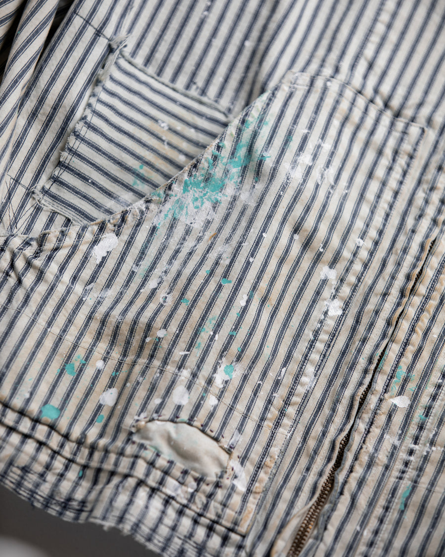 ゆとりある身幅とややクロップド丈でレイヤードを楽しめるデザインにしたヒッコリージャケット。
岡山県製9ozヒッコリーストライプ生地を使用し、ハリのあるしっかりとした風合いが特徴。
全体にエイジングとハードダメージを施し、手作業のステッチ補修とランダムなペンキでリアルな表情に仕上げています。