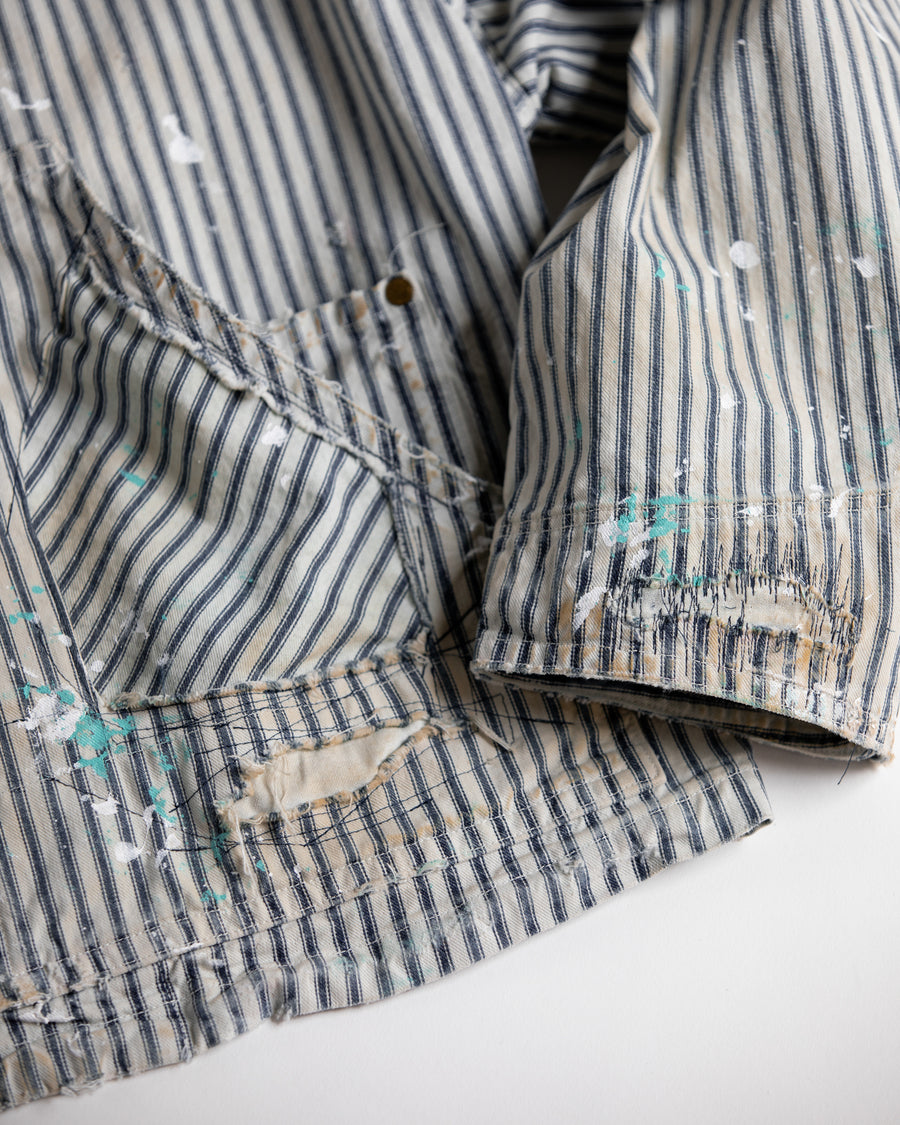 ゆとりある身幅とややクロップド丈でレイヤードを楽しめるデザインにしたヒッコリージャケット。
岡山県製9ozヒッコリーストライプ生地を使用し、ハリのあるしっかりとした風合いが特徴。
全体にエイジングとハードダメージを施し、手作業のステッチ補修とランダムなペンキでリアルな表情に仕上げています。