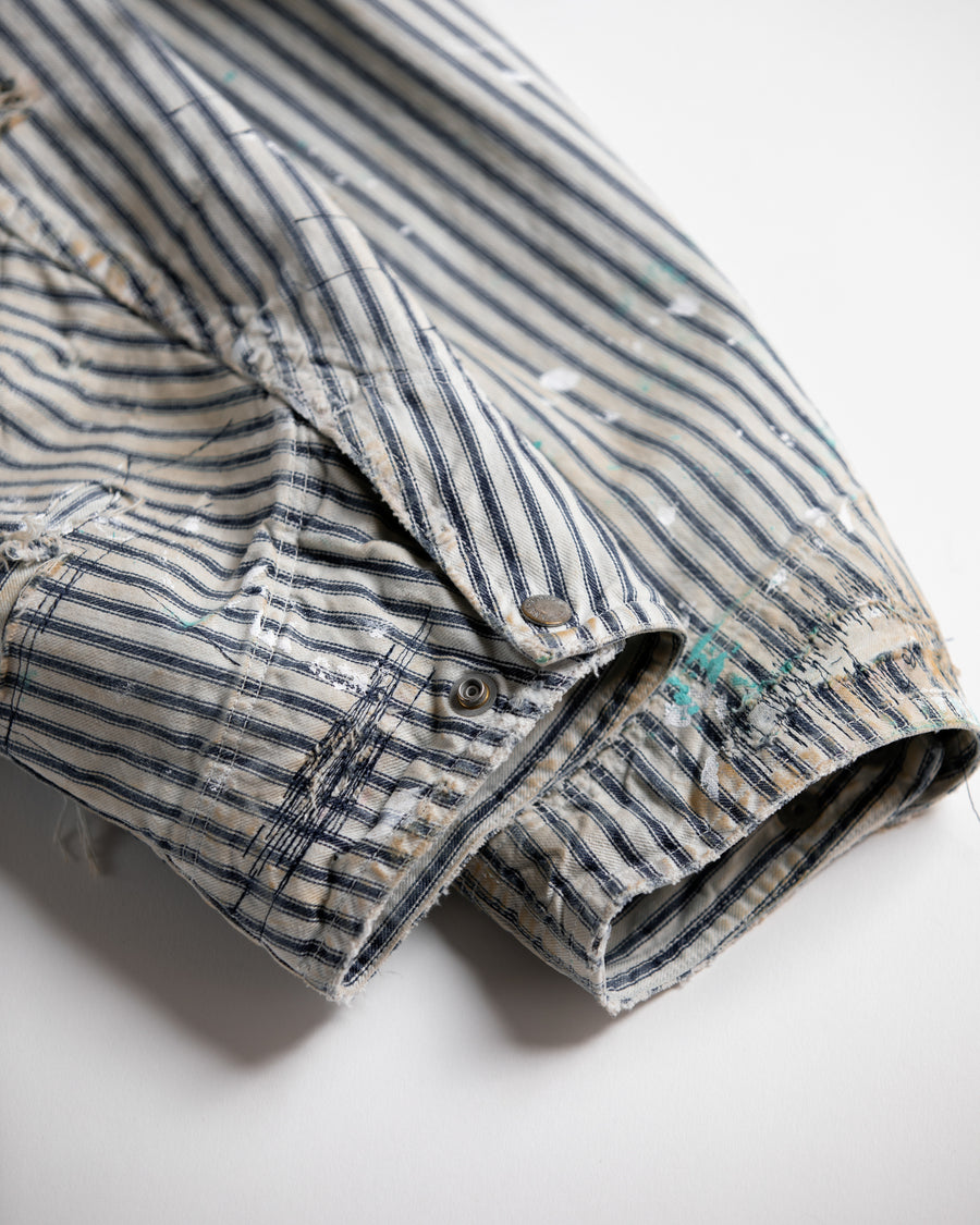 ゆとりある身幅とややクロップド丈でレイヤードを楽しめるデザインにしたヒッコリージャケット。
岡山県製9ozヒッコリーストライプ生地を使用し、ハリのあるしっかりとした風合いが特徴。
全体にエイジングとハードダメージを施し、手作業のステッチ補修とランダムなペンキでリアルな表情に仕上げています。