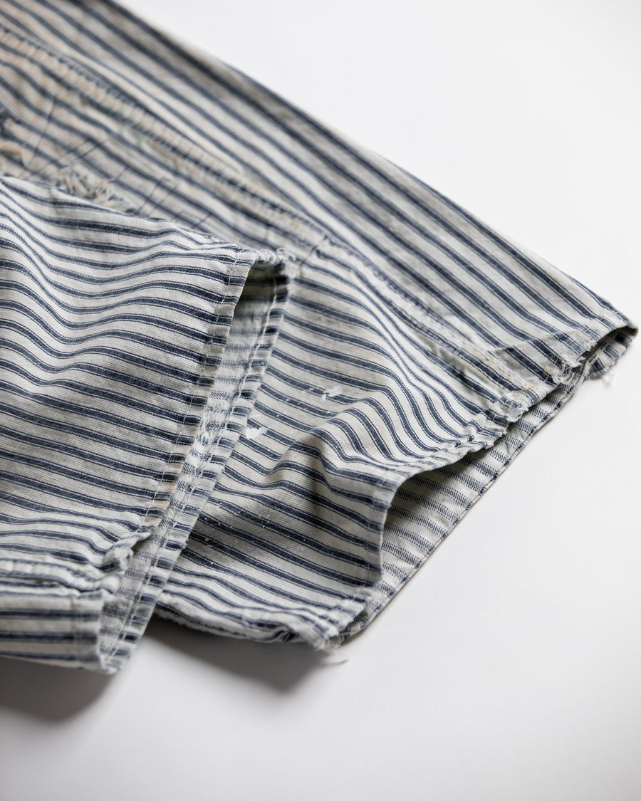 過去の定番ダブルニーペインターパンツをリファインし、腰回りにゆとりを持たせたワイドストレートシルエットに仕上げたヒッコリーパンツ。
岡山県井原市製の9ozヒッコリーストライプ生地を使用し、ハリのある風合いが特徴。
全体にエイジングとハードダメージを施し、手作業のステッチ補修やランダムなペンキでリアルな表情を加えています。