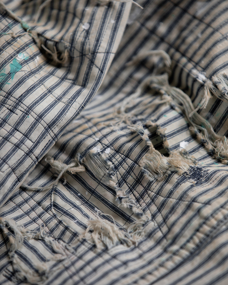 過去の定番ダブルニーペインターパンツをリファインし、腰回りにゆとりを持たせたワイドストレートシルエットに仕上げたヒッコリーパンツ。
岡山県井原市製の9ozヒッコリーストライプ生地を使用し、ハリのある風合いが特徴。
全体にエイジングとハードダメージを施し、手作業のステッチ補修やランダムなペンキでリアルな表情を加えています。