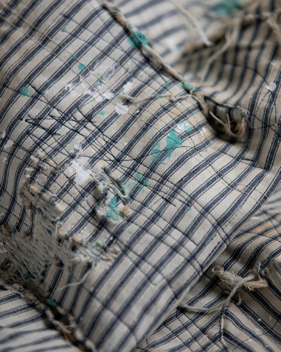 過去の定番ダブルニーペインターパンツをリファインし、腰回りにゆとりを持たせたワイドストレートシルエットに仕上げたヒッコリーパンツ。
岡山県井原市製の9ozヒッコリーストライプ生地を使用し、ハリのある風合いが特徴。
全体にエイジングとハードダメージを施し、手作業のステッチ補修やランダムなペンキでリアルな表情を加えています。