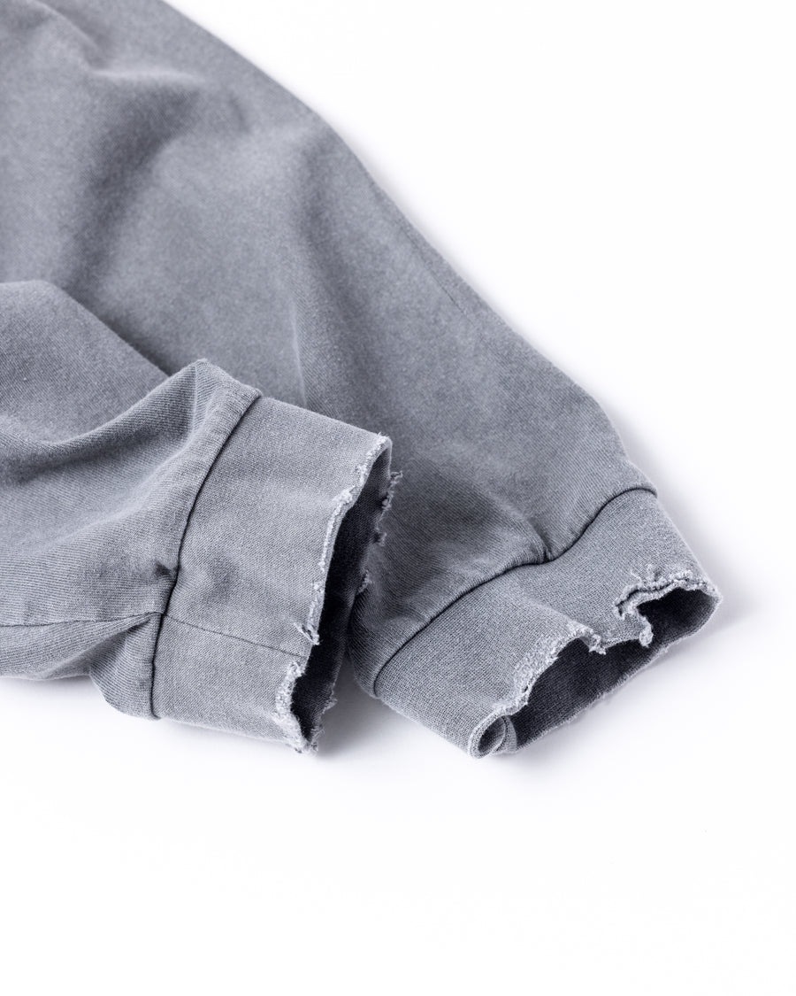 こだわりのオリジナルカラーで仕上げたロングスリーブTシャツ。幾度もの染色テストを重ね、他にはない絶妙な色味を追求しました。素材にはローゲージで編み立てたコットン天竺を採用し、程よい厚みとクリアな質感を両立。特殊顔料染めを施すことで、グレーの柔らかな発色の中に奥行きのある表情と、独特なこなれ感を引き出しています。

A long-sleeve T-shirt featuring a meticulously developed original color. Crafted from a relatively low-gauge cotton jersey for a clean yet structured look. This GRAY piece is treated with a special pigment dye, achieving a unique depth of color and a sophisticated, lived-in texture that results from extensive color testing.