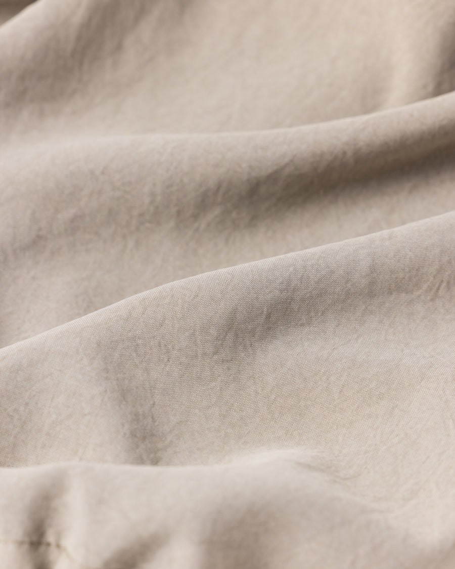 ポリエステル100％ながら、綿のような質感と軽量性を備えた高機能素材を採用。タスラン加工糸によるポリエステルオックスは、シワになりにくく速乾性にも優れています。染色が困難なポリエステルに特殊顔料染めを施すことで、化繊特有の光沢を抑え、ナチュラルで奥行きのある絶妙なフェード感と落ち着いた表情を実現しました。

High-performance polyester oxford with a cotton-like touch, offering quick-dry and wrinkle-resistant benefits. This GRAY BEIGE item features a special pigment dye—a rare process for polyester—achieving a sophisticated, faded texture and a matte finish that perfectly balances technical utility with a natural, lived-in aesthetic.