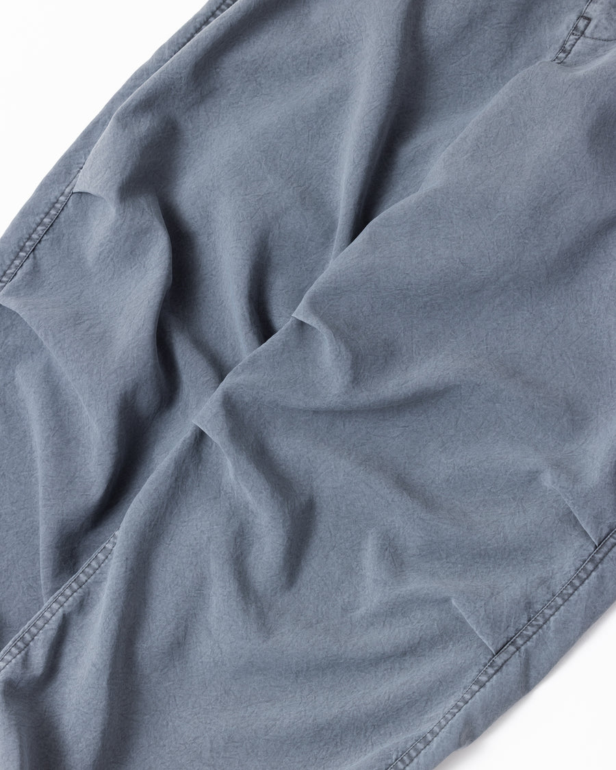 ポリエステル100％ながら、綿のような質感と軽量性を備えた高機能素材を採用。タスラン加工糸によるポリエステルオックスは、シワになりにくく速乾性にも優れています。染色が困難なポリエステルに特殊顔料染めを施すことで、化繊特有の光沢を抑え、ナチュラルで奥行きのある絶妙なフェード感と落ち着いた表情を実現しました。

High-performance polyester oxford with a cotton-like touch, offering quick-dry and wrinkle-resistant benefits. This GRAY BLUE item features a special pigment dye—a rare process for polyester—achieving a sophisticated, faded texture and a matte finish that perfectly balances technical utility with a natural, lived-in aesthetic.