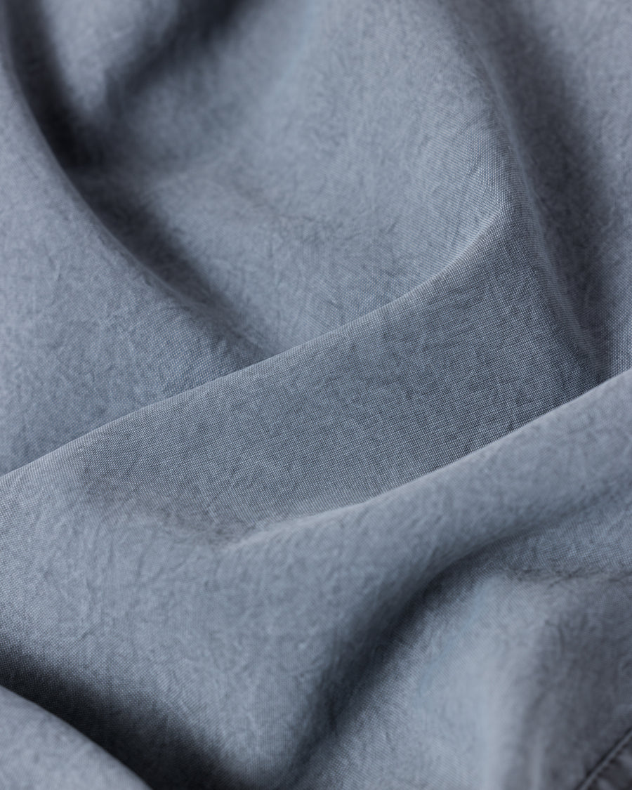 ポリエステル100％ながら、綿のような質感と軽量性を備えた高機能素材を採用。タスラン加工糸によるポリエステルオックスは、シワになりにくく速乾性にも優れています。染色が困難なポリエステルに特殊顔料染めを施すことで、化繊特有の光沢を抑え、ナチュラルで奥行きのある絶妙なフェード感と落ち着いた表情を実現しました。

High-performance polyester oxford with a cotton-like touch, offering quick-dry and wrinkle-resistant benefits. This GRAY BLUE item features a special pigment dye—a rare process for polyester—achieving a sophisticated, faded texture and a matte finish that perfectly balances technical utility with a natural, lived-in aesthetic.