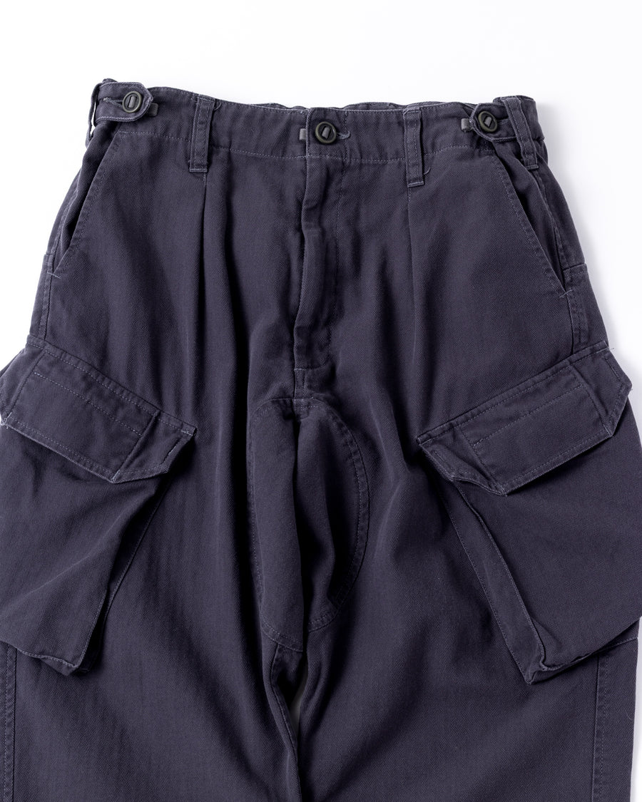 ミリタリートラウザーズをベースに、シルエットを現代的にリファイン。印象的な斜めのカーゴポケットが、立体感と実用性を両立させています。裾にかけて緩やかに絞られたテーパードラインにより、無骨ながらも洗練された印象に。素材には肌馴染みの良い10sヘリンボンを採用し、ストーンバイオウォッシュで柔らかな風合いとこなれ感を引き出しました。

Military trousers refined with a modern tapered silhouette. The distinctive slanted cargo pockets offer both practical utility and a structured look. Crafted from soft, classic 10s herringbone, this CHARCOAL pair has been treated with a stone bio-wash, providing a comfortable, worn-in texture and a sophisticated take on rugged style.
