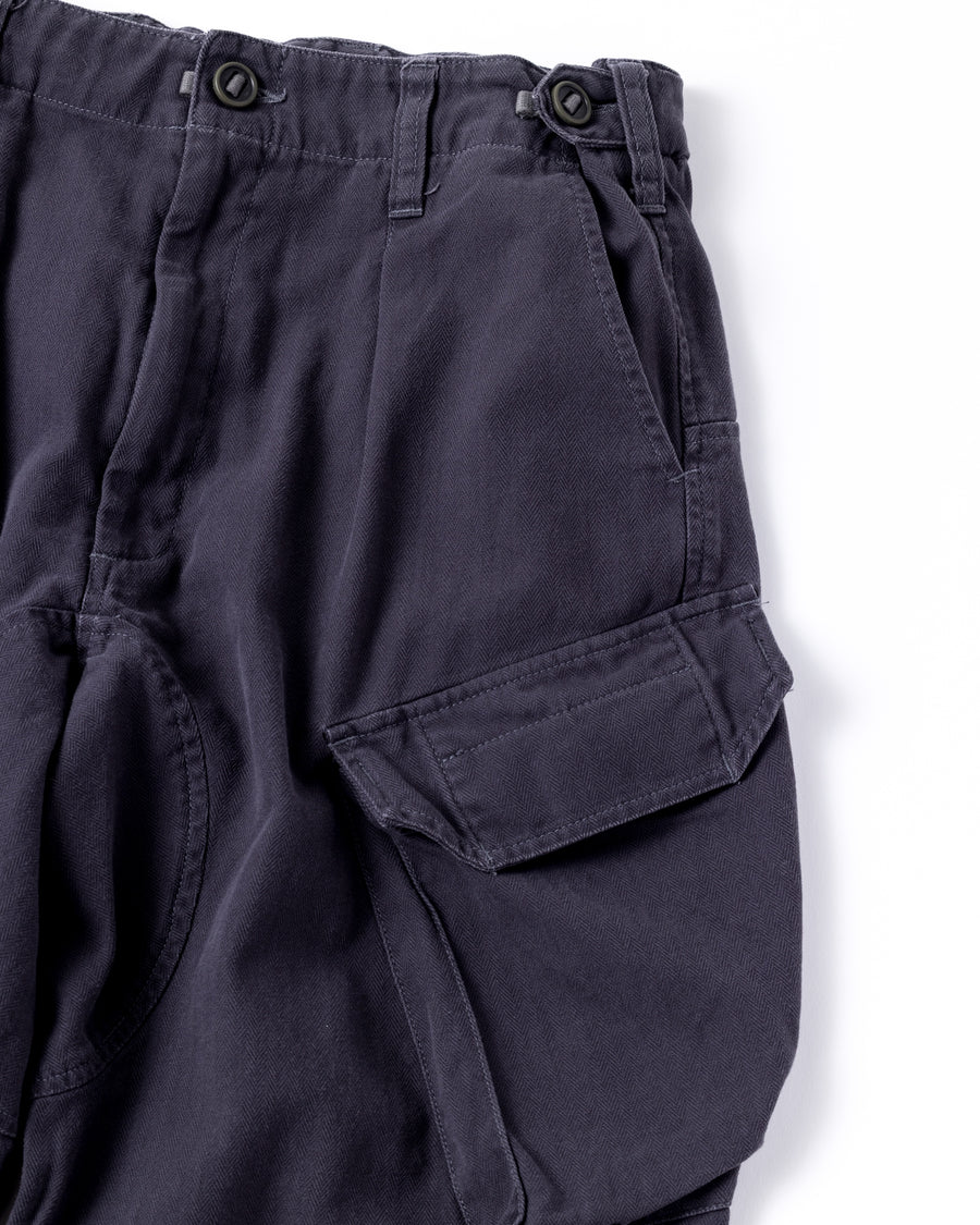 ミリタリートラウザーズをベースに、シルエットを現代的にリファイン。印象的な斜めのカーゴポケットが、立体感と実用性を両立させています。裾にかけて緩やかに絞られたテーパードラインにより、無骨ながらも洗練された印象に。素材には肌馴染みの良い10sヘリンボンを採用し、ストーンバイオウォッシュで柔らかな風合いとこなれ感を引き出しました。

Military trousers refined with a modern tapered silhouette. The distinctive slanted cargo pockets offer both practical utility and a structured look. Crafted from soft, classic 10s herringbone, this CHARCOAL pair has been treated with a stone bio-wash, providing a comfortable, worn-in texture and a sophisticated take on rugged style.