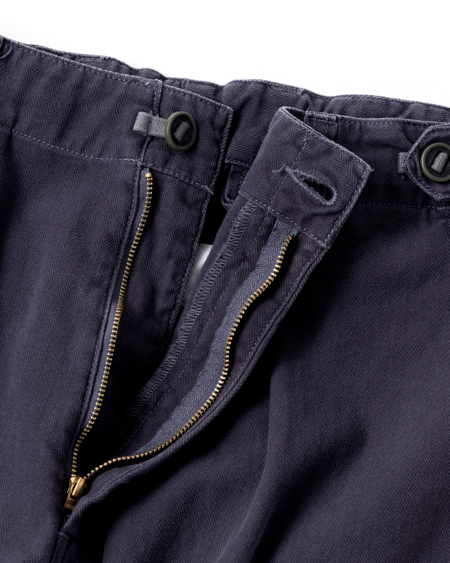 ミリタリートラウザーズをベースに、シルエットを現代的にリファイン。印象的な斜めのカーゴポケットが、立体感と実用性を両立させています。裾にかけて緩やかに絞られたテーパードラインにより、無骨ながらも洗練された印象に。素材には肌馴染みの良い10sヘリンボンを採用し、ストーンバイオウォッシュで柔らかな風合いとこなれ感を引き出しました。

Military trousers refined with a modern tapered silhouette. The distinctive slanted cargo pockets offer both practical utility and a structured look. Crafted from soft, classic 10s herringbone, this CHARCOAL pair has been treated with a stone bio-wash, providing a comfortable, worn-in texture and a sophisticated take on rugged style.