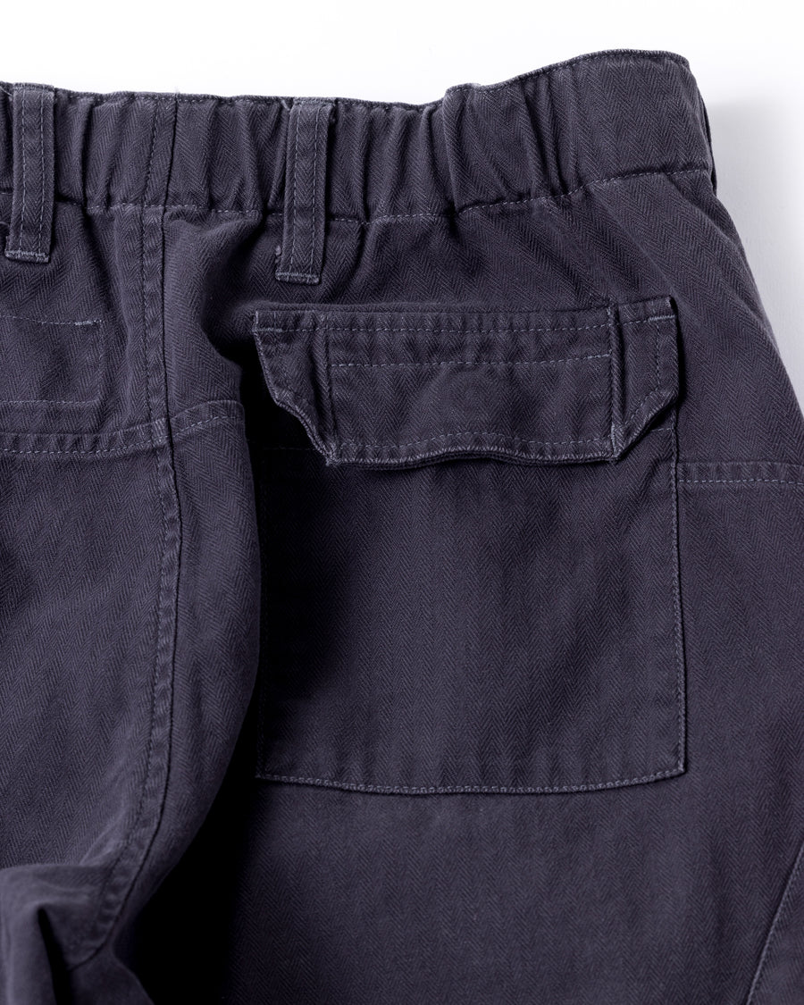ミリタリートラウザーズをベースに、シルエットを現代的にリファイン。印象的な斜めのカーゴポケットが、立体感と実用性を両立させています。裾にかけて緩やかに絞られたテーパードラインにより、無骨ながらも洗練された印象に。素材には肌馴染みの良い10sヘリンボンを採用し、ストーンバイオウォッシュで柔らかな風合いとこなれ感を引き出しました。

Military trousers refined with a modern tapered silhouette. The distinctive slanted cargo pockets offer both practical utility and a structured look. Crafted from soft, classic 10s herringbone, this CHARCOAL pair has been treated with a stone bio-wash, providing a comfortable, worn-in texture and a sophisticated take on rugged style.