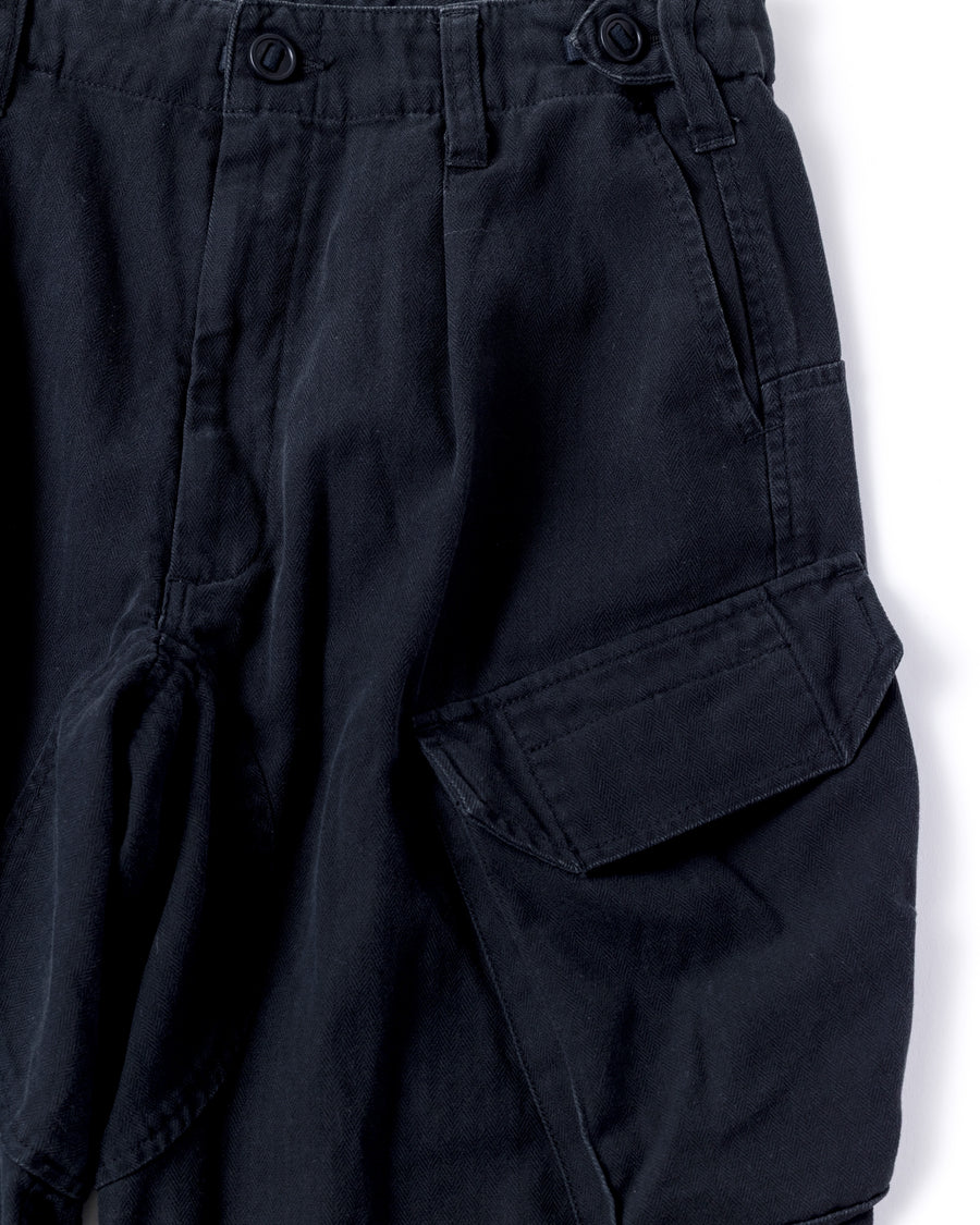 ミリタリートラウザーズをベースに、シルエットを現代的にリファイン。印象的な斜めのカーゴポケットが、立体感と実用性を両立させています。裾にかけて緩やかに絞られたテーパードラインにより、無骨ながらも洗練された印象に。素材には肌馴染みの良い10sヘリンボンを採用し、ストーンバイオウォッシュで柔らかな風合いとこなれ感を引き出しました。

Military trousers refined with a modern tapered silhouette. The distinctive slanted cargo pockets offer both practical utility and a structured look. Crafted from soft, classic 10s herringbone, this BLACK pair has been treated with a stone bio-wash, providing a comfortable, worn-in texture and a sophisticated take on rugged style.