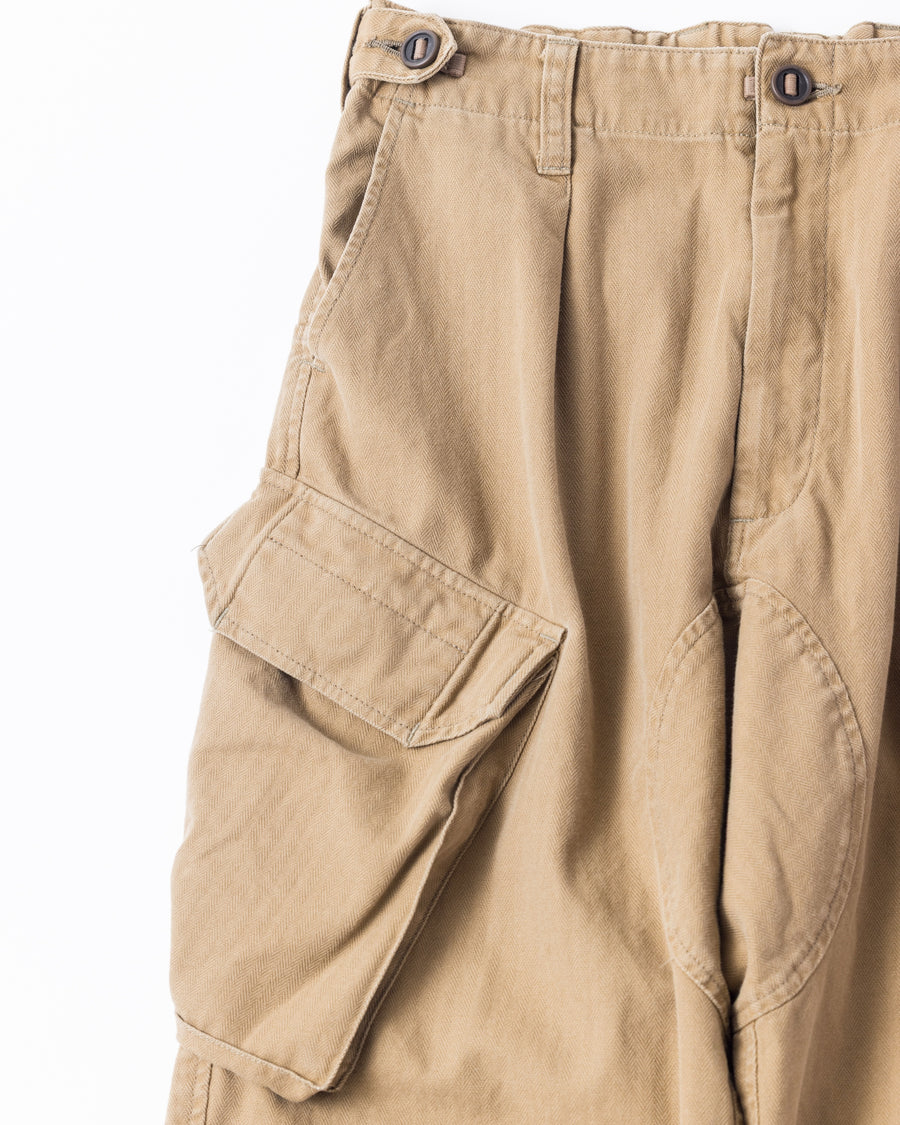 ミリタリートラウザーズをベースに、シルエットを現代的にリファイン。印象的な斜めのカーゴポケットが、立体感と実用性を両立させています。裾にかけて緩やかに絞られたテーパードラインにより、無骨ながらも洗練された印象に。素材には肌馴染みの良い10sヘリンボンを採用し、ストーンバイオウォッシュで柔らかな風合いとこなれ感を引き出しました。

Military trousers refined with a modern tapered silhouette. The distinctive slanted cargo pockets offer both practical utility and a structured look. Crafted from soft, classic 10s herringbone, this KHAKI pair has been treated with a stone bio-wash, providing a comfortable, worn-in texture and a sophisticated take on rugged style.