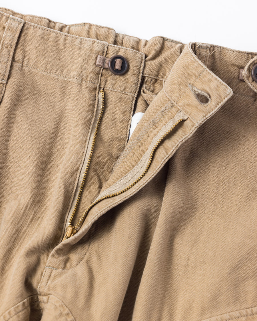 ミリタリートラウザーズをベースに、シルエットを現代的にリファイン。印象的な斜めのカーゴポケットが、立体感と実用性を両立させています。裾にかけて緩やかに絞られたテーパードラインにより、無骨ながらも洗練された印象に。素材には肌馴染みの良い10sヘリンボンを採用し、ストーンバイオウォッシュで柔らかな風合いとこなれ感を引き出しました。

Military trousers refined with a modern tapered silhouette. The distinctive slanted cargo pockets offer both practical utility and a structured look. Crafted from soft, classic 10s herringbone, this KHAKI pair has been treated with a stone bio-wash, providing a comfortable, worn-in texture and a sophisticated take on rugged style.
