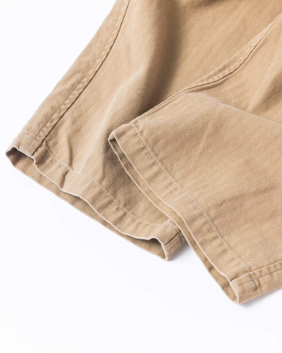 ミリタリートラウザーズをベースに、シルエットを現代的にリファイン。印象的な斜めのカーゴポケットが、立体感と実用性を両立させています。裾にかけて緩やかに絞られたテーパードラインにより、無骨ながらも洗練された印象に。素材には肌馴染みの良い10sヘリンボンを採用し、ストーンバイオウォッシュで柔らかな風合いとこなれ感を引き出しました。

Military trousers refined with a modern tapered silhouette. The distinctive slanted cargo pockets offer both practical utility and a structured look. Crafted from soft, classic 10s herringbone, this KHAKI pair has been treated with a stone bio-wash, providing a comfortable, worn-in texture and a sophisticated take on rugged style.