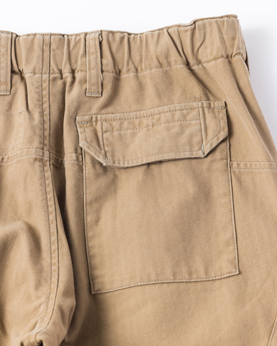 ミリタリートラウザーズをベースに、シルエットを現代的にリファイン。印象的な斜めのカーゴポケットが、立体感と実用性を両立させています。裾にかけて緩やかに絞られたテーパードラインにより、無骨ながらも洗練された印象に。素材には肌馴染みの良い10sヘリンボンを採用し、ストーンバイオウォッシュで柔らかな風合いとこなれ感を引き出しました。

Military trousers refined with a modern tapered silhouette. The distinctive slanted cargo pockets offer both practical utility and a structured look. Crafted from soft, classic 10s herringbone, this KHAKI pair has been treated with a stone bio-wash, providing a comfortable, worn-in texture and a sophisticated take on rugged style.