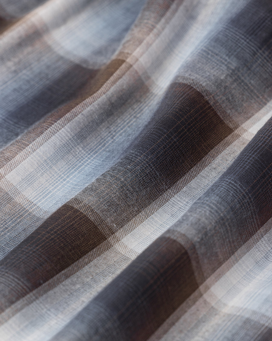 オンブレチェック柄が目を惹くオープンカラーシャツ。生地が持つ自然なドレープ感を活かし、リラックス感のあるゆとりを持たせたシルエットに仕上げました。素材にはタテ・ヨコ共にレーヨン糸を使用したレーヨンチェックを採用。非常に優れた落ち感と、袖を通した瞬間に感じる滑らかで心地よい肌触りが、上質なリラックススタイルを演出します。

An open-collar shirt featuring a classic ombre check pattern. The relaxed silhouette highlights the natural drape and fluid movement of the fabric. Crafted from a high-quality rayon check weave, this BLUE CHECK piece is characterized by its exceptional softness and smooth touch, offering a sophisticated look with an effortlessly comfortable feel.