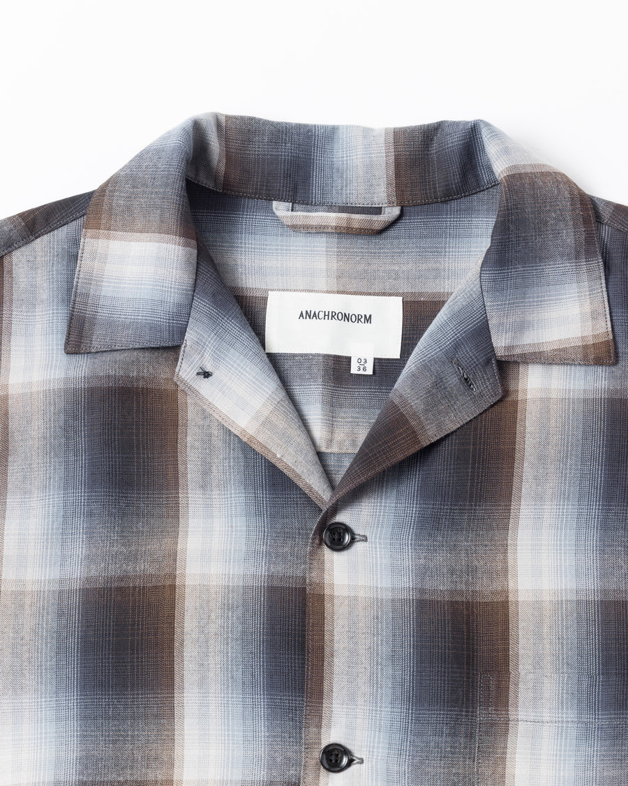オンブレチェック柄が目を惹くオープンカラーシャツ。生地が持つ自然なドレープ感を活かし、リラックス感のあるゆとりを持たせたシルエットに仕上げました。素材にはタテ・ヨコ共にレーヨン糸を使用したレーヨンチェックを採用。非常に優れた落ち感と、袖を通した瞬間に感じる滑らかで心地よい肌触りが、上質なリラックススタイルを演出します。

An open-collar shirt featuring a classic ombre check pattern. The relaxed silhouette highlights the natural drape and fluid movement of the fabric. Crafted from a high-quality rayon check weave, this BLUE CHECK piece is characterized by its exceptional softness and smooth touch, offering a sophisticated look with an effortlessly comfortable feel.