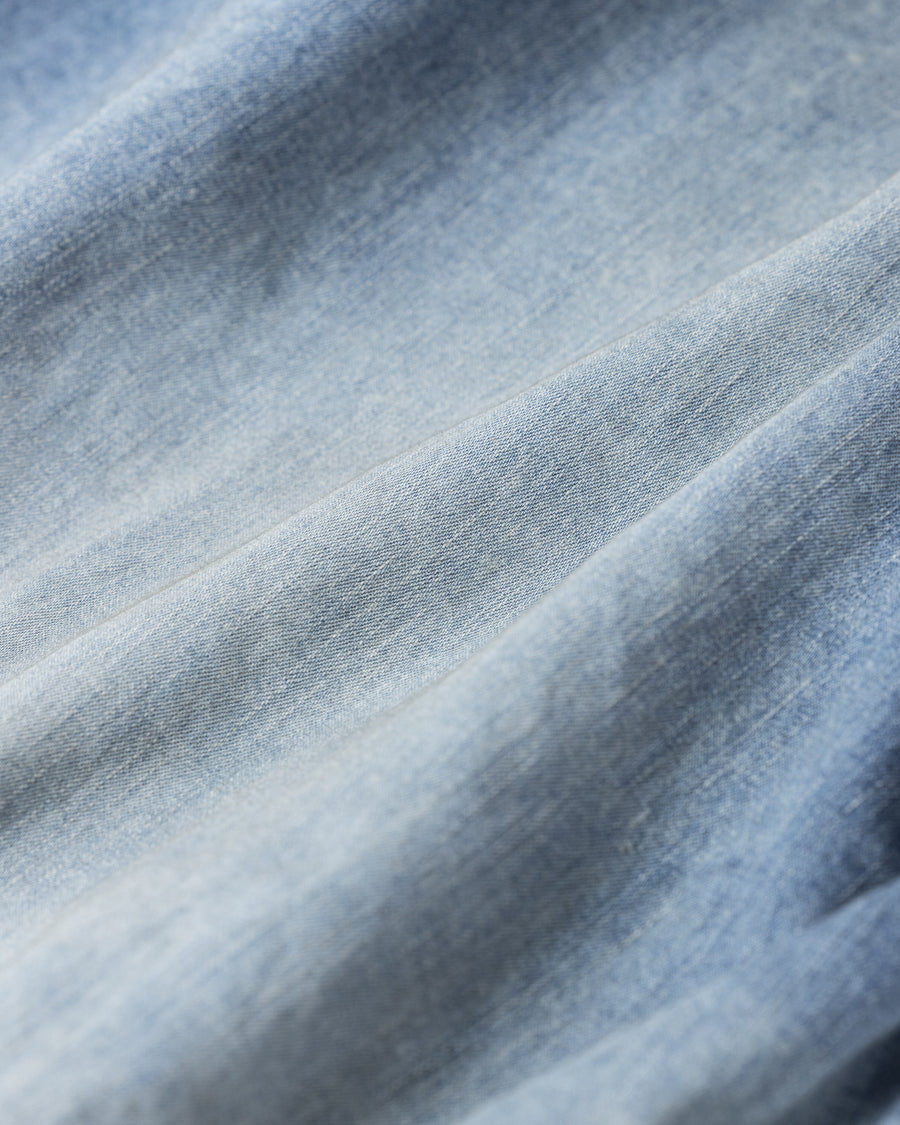フード口のボタンの開閉により、首まわりのニュアンスを変えて楽しめる一着。素材には、経糸にコットンムラ糸、緯糸に綿麻混紡糸を使用した綿麻6ozデニムを採用しました。シャープなムラ感とリネン混ならではの粗野な風合いが、ヴィンテージの魅力を引き立てます。エイジング加工を施すことで、全体にリアリティのあるアタリ感を出し、長年着込んだような深みのある表情に仕上げました。A versatile piece featuring adjustable hood buttons to create a clean or relaxed neckline. Crafted from 6oz cotton-linen denim, the fabric combines sharp slub textures with a rustic linen feel for an authentic vintage character. Treated with an aging process to create realistic wear and fade, this INDIGO garment offers a sophisti