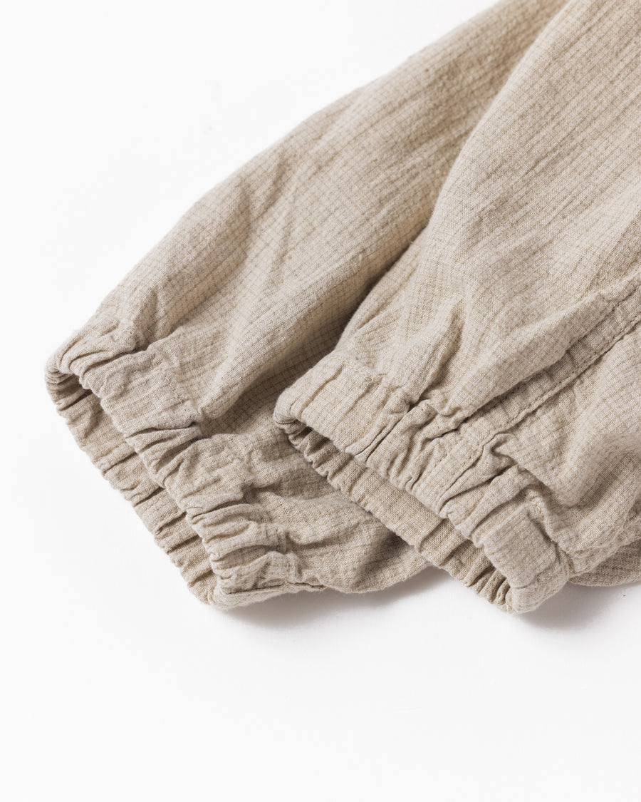 フード口のボタンの開閉により、首周りのニュアンスを自在に調整できる一着。素材には、麻カスや節を活かしたネップ糸を織り交ぜたコットンリネンチェックを採用しました。ドライタッチな生地にワンウォッシュを施すことで、麻特有のハリ感を残しつつ、肌馴染みの良い柔らかな風合いと豊かな表情を引き出しています。

This piece features adjustable hood buttons to alternate between a clean look and a relaxed neckline. Crafted from a cotton-linen check weave with rustic nep yarns, it highlights the natural texture of the fibers. The BEIGE fabric is one-washed to balance a crisp, dry touch with a soft, broken-in feel, creating a sophisticated yet comfortable aesthetic.