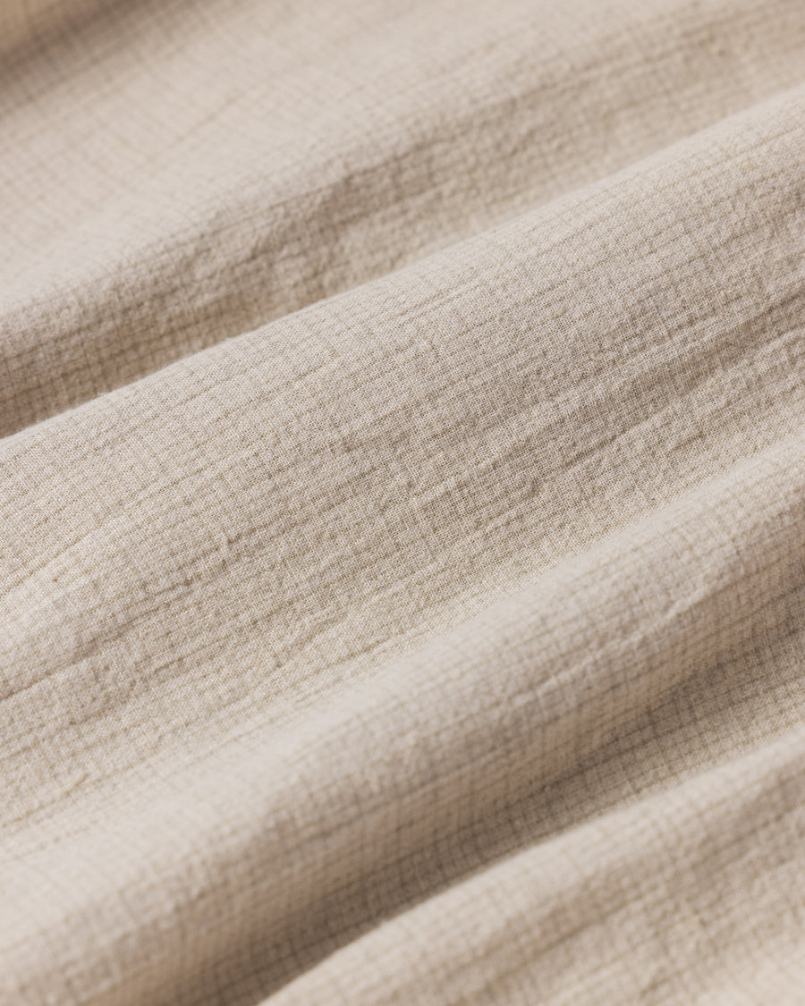 フード口のボタンの開閉により、首周りのニュアンスを自在に調整できる一着。素材には、麻カスや節を活かしたネップ糸を織り交ぜたコットンリネンチェックを採用しました。ドライタッチな生地にワンウォッシュを施すことで、麻特有のハリ感を残しつつ、肌馴染みの良い柔らかな風合いと豊かな表情を引き出しています。

This piece features adjustable hood buttons to alternate between a clean look and a relaxed neckline. Crafted from a cotton-linen check weave with rustic nep yarns, it highlights the natural texture of the fibers. The BEIGE fabric is one-washed to balance a crisp, dry touch with a soft, broken-in feel, creating a sophisticated yet comfortable aesthetic.
