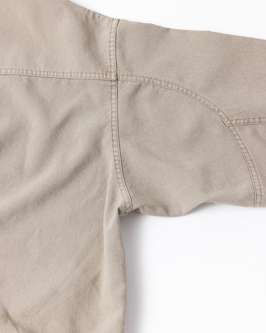 ポリエステル100％でありながら、綿のような質感と軽量性を備えた高機能な一着。タスラン加工糸を使用したポリエステルオックスを採用し、シワになりにくく速乾性に優れたイージーケア性を実現しました。本来染色が困難な素材に特殊顔料染めを施すことで、化繊特有の光沢を抑えた、ナチュラルで奥行きのある絶妙なフェード感を表現しています。

A high-performance piece crafted from polyester oxford, offering a cotton-like touch with lightweight, quick-dry, and wrinkle-resistant properties. This GRAY BEIGE item features a special pigment dye—a rare process for polyester—achieving a sophisticated, faded texture and a matte finish that defies its synthetic origins.