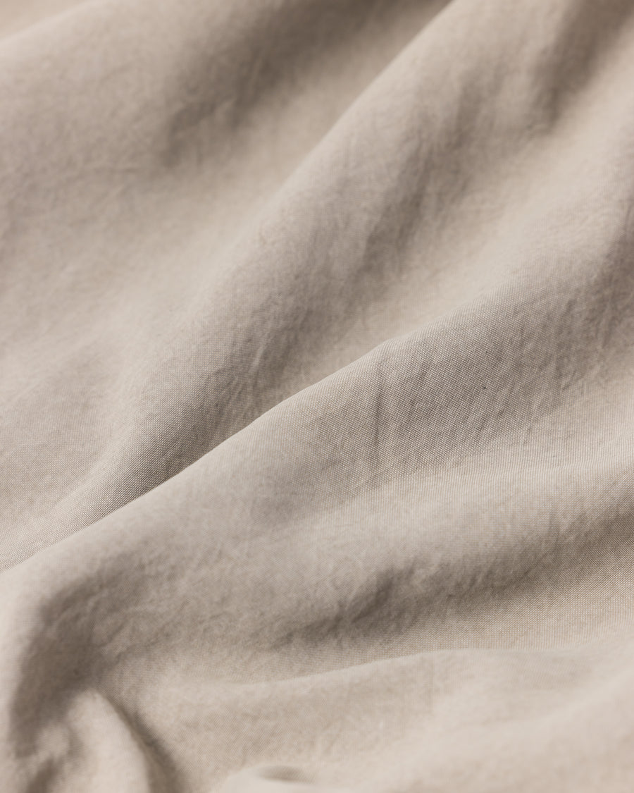 ポリエステル100％でありながら、綿のような質感と軽量性を備えた高機能な一着。タスラン加工糸を使用したポリエステルオックスを採用し、シワになりにくく速乾性に優れたイージーケア性を実現しました。本来染色が困難な素材に特殊顔料染めを施すことで、化繊特有の光沢を抑えた、ナチュラルで奥行きのある絶妙なフェード感を表現しています。

A high-performance piece crafted from polyester oxford, offering a cotton-like touch with lightweight, quick-dry, and wrinkle-resistant properties. This GRAY BEIGE item features a special pigment dye—a rare process for polyester—achieving a sophisticated, faded texture and a matte finish that defies its synthetic origins.