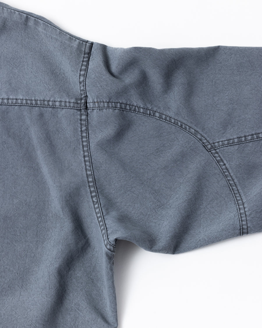 ポリエステル100％でありながら、綿のような質感と軽量性を備えた高機能な一着。タスラン加工糸を使用したポリエステルオックスを採用し、シワになりにくく速乾性に優れたイージーケア性を実現しました。本来染色が困難な素材に特殊顔料染めを施すことで、化繊特有の光沢を抑えた、ナチュラルで奥行きのある絶妙なフェード感を表現しています。

A high-performance piece crafted from polyester oxford, offering a cotton-like touch with lightweight, quick-dry, and wrinkle-resistant properties. This GRAY BLUE item features a special pigment dye—a rare process for polyester—achieving a sophisticated, faded texture and a matte finish that defies its synthetic origins.