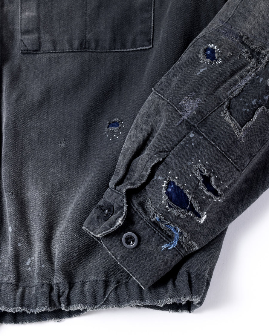 ミリタリーのシャツジャケットを現代的シルエットに更新。裾のドローコードでスタイルに合わせた変化を楽しめます。素材には肌馴染みの良い10sヘリンボンを採用。環境に配慮した特殊エイジング・サンフェード加工とダメージ加工を施すことで、クラシカルな生地にリアリティのある褪色感とヴィンテージライクな佇まいを表現しました。

A modern military shirt jacket with hem drawcords for an adjustable silhouette. Crafted from soft 10s herringbone, this BLACK piece undergoes a special sun-fade and damage process. It achieves a realistic, time-worn vintage look with authentic distressing while minimizing environmental impact through eco-conscious processing.