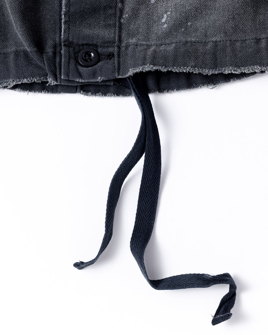 ミリタリーのシャツジャケットを現代的シルエットに更新。裾のドローコードでスタイルに合わせた変化を楽しめます。素材には肌馴染みの良い10sヘリンボンを採用。環境に配慮した特殊エイジング・サンフェード加工とダメージ加工を施すことで、クラシカルな生地にリアリティのある褪色感とヴィンテージライクな佇まいを表現しました。

A modern military shirt jacket with hem drawcords for an adjustable silhouette. Crafted from soft 10s herringbone, this BLACK piece undergoes a special sun-fade and damage process. It achieves a realistic, time-worn vintage look with authentic distressing while minimizing environmental impact through eco-conscious processing.