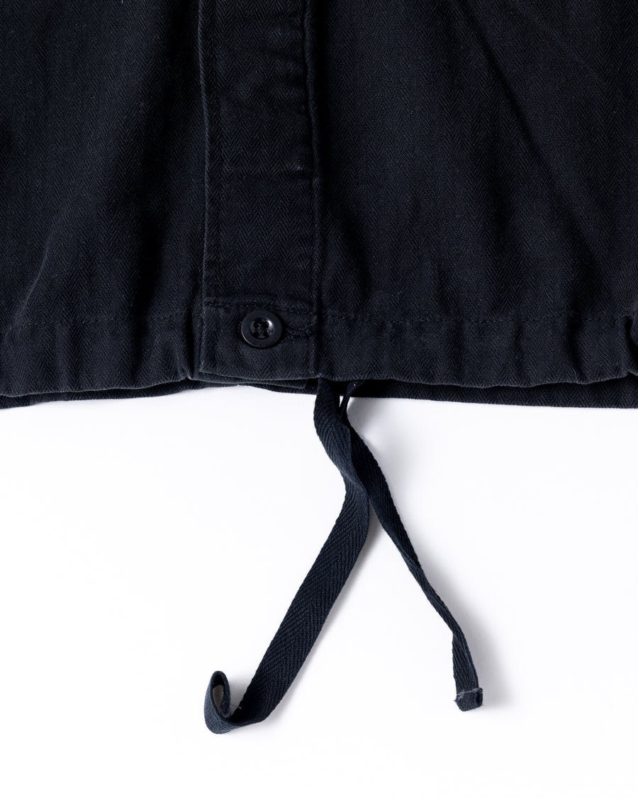 ミリタリーのシャツジャケットを現代的シルエットに更新。裾のドローコードで着丈のニュアンスを自在に調整可能です。素材には、やや甘織りで肌馴染みの良い10sヘリンボンを採用。ストーンバイオウォッシュを施すことで、クラシカルな生地感に柔らかな風合いとこなれ感をプラスした、着回し力の高い一着に仕上げました。

A modern update to the classic military shirt jacket, featuring hem drawcords for an adjustable silhouette. Crafted from 10s herringbone, slightly loose-knitted for a soft, comfortable touch. This BLACK piece has been treated with a stone bio-wash, giving the traditional weave a natural, worn-in texture and a sophisticated casual feel.