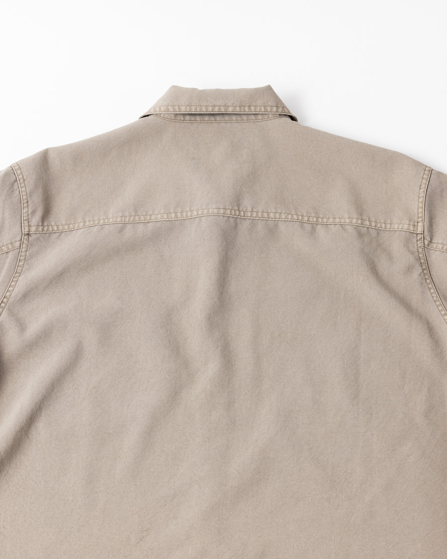 ポリエステル100％ながら、綿のような質感と軽量性を備えた高機能素材を採用。タスラン加工糸を使用したポリエステルオックスは、シワになりにくく速乾性にも優れています。本来染色が困難な素材に特殊顔料染めを施すことで、化繊特有の光沢を抑え、ナチュラルで奥行きのある絶妙なフェード感と落ち着いた表情を実現しました。

A high-performance piece crafted from polyester oxford, offering a cotton-like touch with quick-dry and wrinkle-resistant benefits. This GRAY BEIGE item features a special pigment dye—a rare process for polyester—achieving a sophisticated, faded texture and a matte finish that perfectly balances technical utility with a natural, lived-in aesthetic.
