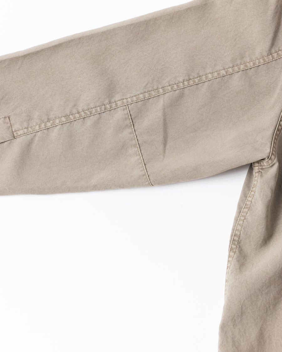 ポリエステル100％ながら、綿のような質感と軽量性を備えた高機能素材を採用。タスラン加工糸を使用したポリエステルオックスは、シワになりにくく速乾性にも優れています。本来染色が困難な素材に特殊顔料染めを施すことで、化繊特有の光沢を抑え、ナチュラルで奥行きのある絶妙なフェード感と落ち着いた表情を実現しました。

A high-performance piece crafted from polyester oxford, offering a cotton-like touch with quick-dry and wrinkle-resistant benefits. This GRAY BEIGE item features a special pigment dye—a rare process for polyester—achieving a sophisticated, faded texture and a matte finish that perfectly balances technical utility with a natural, lived-in aesthetic.