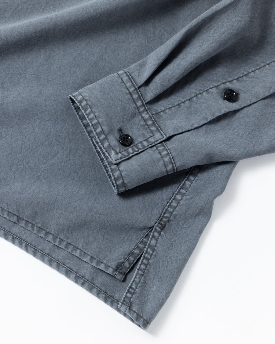 ポリエステル100％ながら、綿のような質感と軽量性を備えた高機能素材を採用。タスラン加工糸を使用したポリエステルオックスは、シワになりにくく速乾性にも優れています。本来染色が困難な素材に特殊顔料染めを施すことで、化繊特有の光沢を抑え、ナチュラルで奥行きのある絶妙なフェード感と落ち着いた表情を実現しました。

A high-performance piece crafted from polyester oxford, offering a cotton-like touch with quick-dry and wrinkle-resistant benefits. This GRAY BEIGE item features a special pigment dye—a rare process for polyester—achieving a sophisticated, faded texture and a matte finish that perfectly balances technical utility with a natural, lived-in aesthetic.