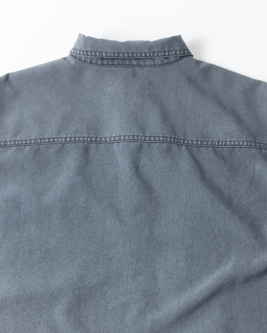 ポリエステル100％ながら、綿のような質感と軽量性を備えた高機能素材を採用。タスラン加工糸を使用したポリエステルオックスは、シワになりにくく速乾性にも優れています。本来染色が困難な素材に特殊顔料染めを施すことで、化繊特有の光沢を抑え、ナチュラルで奥行きのある絶妙なフェード感と落ち着いた表情を実現しました。

A high-performance piece crafted from polyester oxford, offering a cotton-like touch with quick-dry and wrinkle-resistant benefits. This GRAY BLUE item features a special pigment dye—a rare process for polyester—achieving a sophisticated, faded texture and a matte finish that perfectly balances technical utility with a natural, lived-in aesthetic.