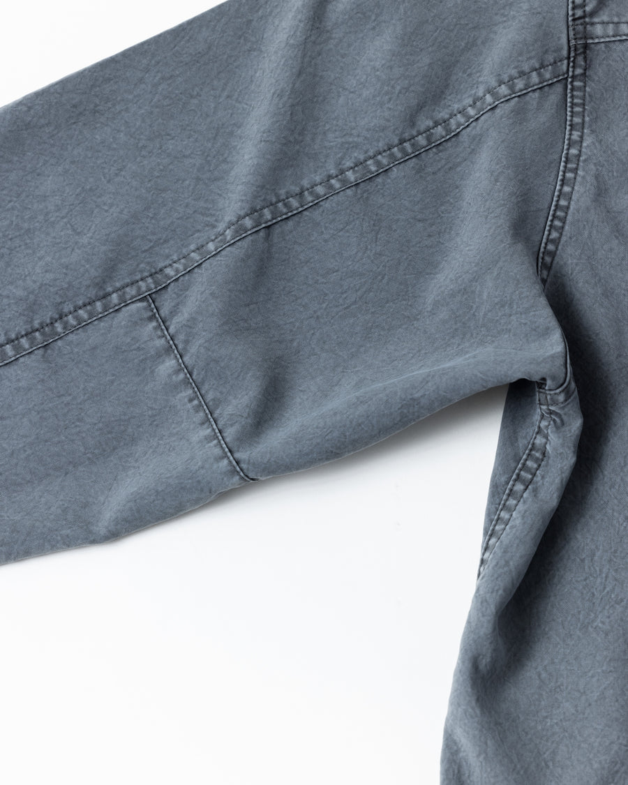 ポリエステル100％ながら、綿のような質感と軽量性を備えた高機能素材を採用。タスラン加工糸を使用したポリエステルオックスは、シワになりにくく速乾性にも優れています。本来染色が困難な素材に特殊顔料染めを施すことで、化繊特有の光沢を抑え、ナチュラルで奥行きのある絶妙なフェード感と落ち着いた表情を実現しました。

A high-performance piece crafted from polyester oxford, offering a cotton-like touch with quick-dry and wrinkle-resistant benefits. This GRAY BLUE item features a special pigment dye—a rare process for polyester—achieving a sophisticated, faded texture and a matte finish that perfectly balances technical utility with a natural, lived-in aesthetic.