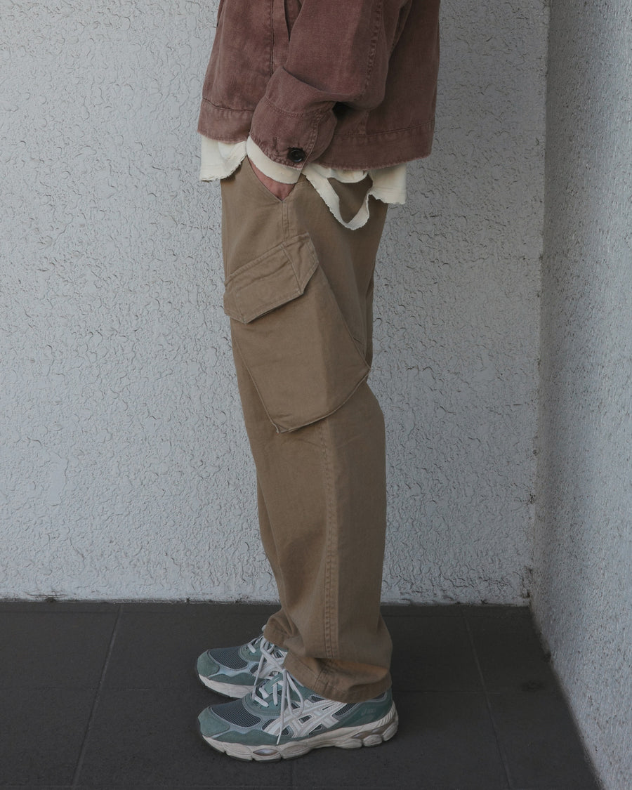 ミリタリートラウザーズをベースに、シルエットを現代的にリファイン。印象的な斜めのカーゴポケットが、立体感と実用性を両立させています。裾にかけて緩やかに絞られたテーパードラインにより、無骨ながらも洗練された印象に。素材には肌馴染みの良い10sヘリンボンを採用し、ストーンバイオウォッシュで柔らかな風合いとこなれ感を引き出しました。

Military trousers refined with a modern tapered silhouette. The distinctive slanted cargo pockets offer both practical utility and a structured look. Crafted from soft, classic 10s herringbone, this KHAKI pair has been treated with a stone bio-wash, providing a comfortable, worn-in texture and a sophisticated take on rugged style.