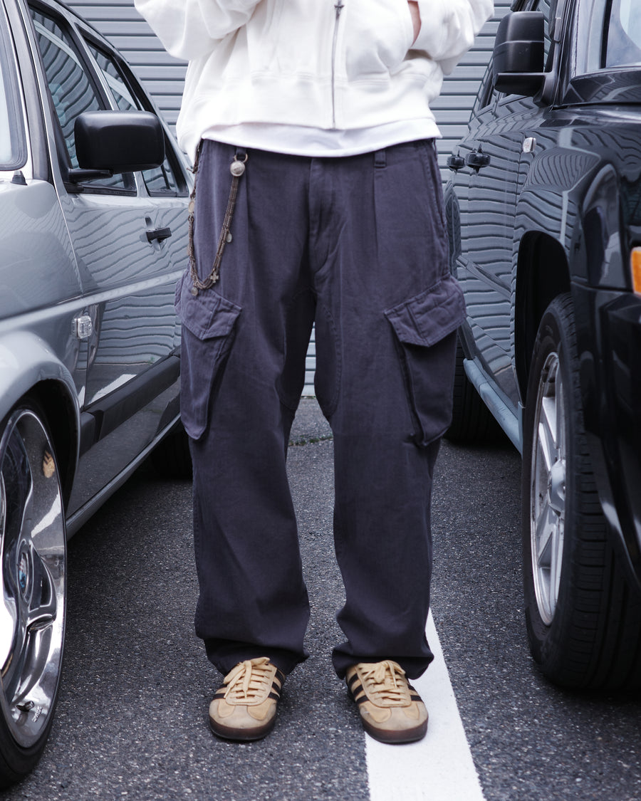 ミリタリートラウザーズをベースに、シルエットを現代的にリファイン。印象的な斜めのカーゴポケットが、立体感と実用性を両立させています。裾にかけて緩やかに絞られたテーパードラインにより、無骨ながらも洗練された印象に。素材には肌馴染みの良い10sヘリンボンを採用し、ストーンバイオウォッシュで柔らかな風合いとこなれ感を引き出しました。

Military trousers refined with a modern tapered silhouette. The distinctive slanted cargo pockets offer both practical utility and a structured look. Crafted from soft, classic 10s herringbone, this CHARCOAL pair has been treated with a stone bio-wash, providing a comfortable, worn-in texture and a sophisticated take on rugged style.