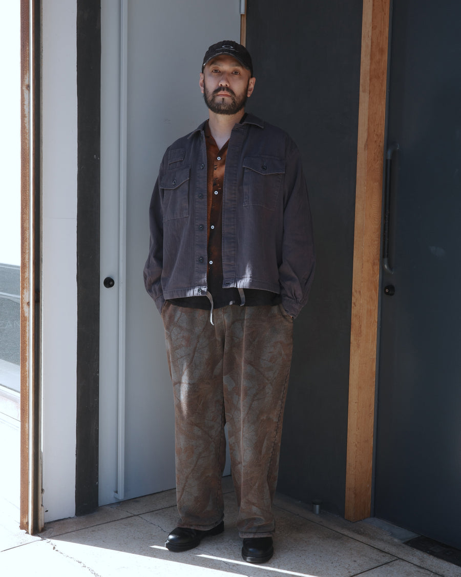 ミリタリーのシャツジャケットを現代的シルエットに更新。裾のドローコードで着丈のニュアンスを自在に調整可能です。素材には、やや甘織りで肌馴染みの良い10sヘリンボンを採用。ストーンバイオウォッシュを施すことで、クラシカルな生地感に柔らかな風合いとこなれ感をプラスした、着回し力の高い一着に仕上げました。

A modern update to the classic military shirt jacket, featuring hem drawcords for an adjustable silhouette. Crafted from 10s herringbone, slightly loose-knitted for a soft, comfortable touch. This BLACK piece has been treated with a stone bio-wash, giving the traditional weave a natural, worn-in texture and a sophisticated casual feel.