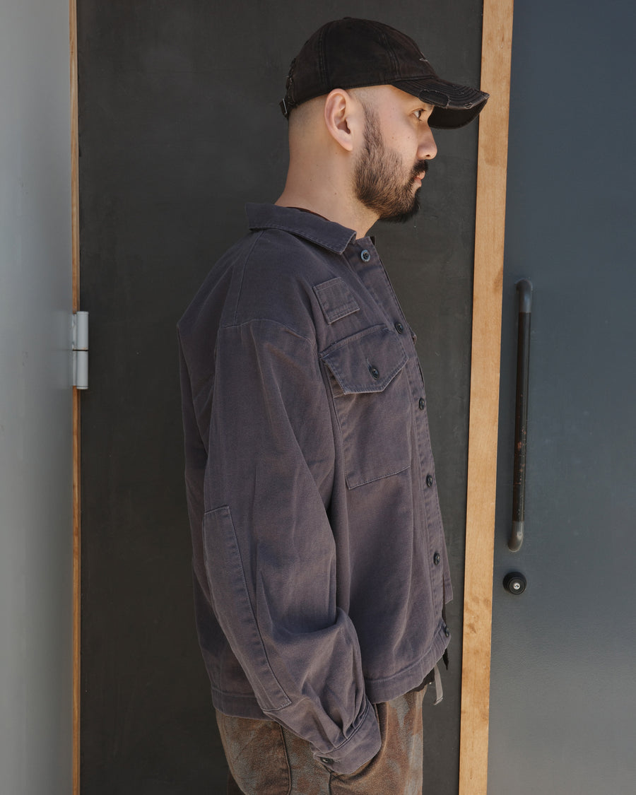 ミリタリーのシャツジャケットを現代的シルエットに更新。裾のドローコードで着丈のニュアンスを自在に調整可能です。素材には、やや甘織りで肌馴染みの良い10sヘリンボンを採用。ストーンバイオウォッシュを施すことで、クラシカルな生地感に柔らかな風合いとこなれ感をプラスした、着回し力の高い一着に仕上げました。

A modern update to the classic military shirt jacket, featuring hem drawcords for an adjustable silhouette. Crafted from 10s herringbone, slightly loose-knitted for a soft, comfortable touch. This BLACK piece has been treated with a stone bio-wash, giving the traditional weave a natural, worn-in texture and a sophisticated casual feel.