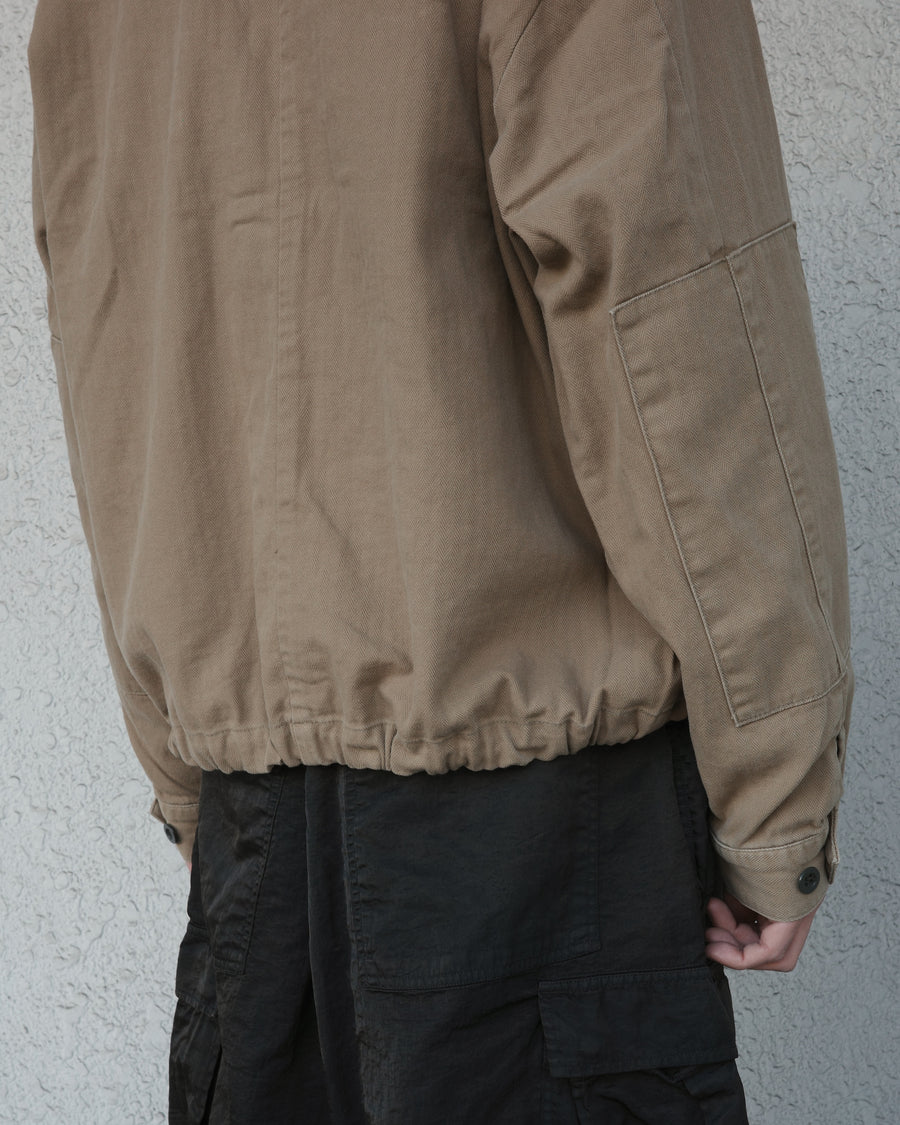ミリタリーのシャツジャケットを現代的シルエットに更新。裾のドローコードで着丈のニュアンスを自在に調整可能です。素材には、やや甘織りで肌馴染みの良い10sヘリンボンを採用。ストーンバイオウォッシュを施すことで、クラシカルな生地感に柔らかな風合いとこなれ感をプラスした、着回し力の高い一着に仕上げました。

A modern update to the classic military shirt jacket, featuring hem drawcords for an adjustable silhouette. Crafted from 10s herringbone, slightly loose-knitted for a soft, comfortable touch. This KHAKI piece has been treated with a stone bio-wash, giving the traditional weave a natural, worn-in texture and a sophisticated casual feel.