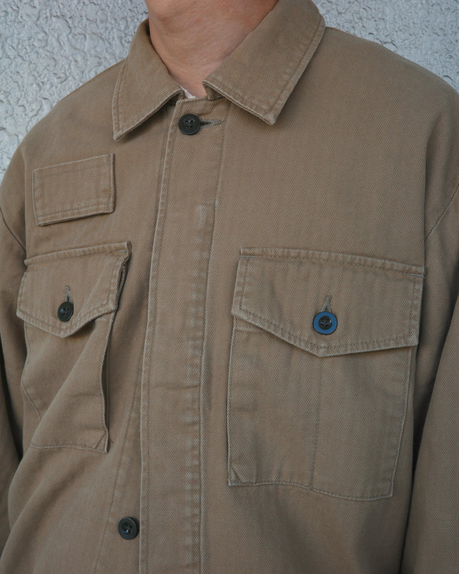 ミリタリーのシャツジャケットを現代的シルエットに更新。裾のドローコードで着丈のニュアンスを自在に調整可能です。素材には、やや甘織りで肌馴染みの良い10sヘリンボンを採用。ストーンバイオウォッシュを施すことで、クラシカルな生地感に柔らかな風合いとこなれ感をプラスした、着回し力の高い一着に仕上げました。

A modern update to the classic military shirt jacket, featuring hem drawcords for an adjustable silhouette. Crafted from 10s herringbone, slightly loose-knitted for a soft, comfortable touch. This KHAKI piece has been treated with a stone bio-wash, giving the traditional weave a natural, worn-in texture and a sophisticated casual feel.