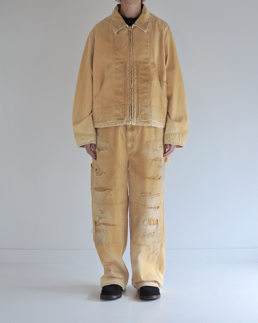 シルエットはゆとりのある身幅とややクロップド丈で設計しており、イエローカラーの鮮やかなトーンがレイヤードスタイルをより引き立てます。インナーアイテムとの重ね着がしやすいバランスに仕上げています。
生地には頒布の中で最も薄手の11号帆布を採用しており、強度・耐久性に優れるだけでなく、着用を重ねるごとにアタリなどの経年変化を楽しめる素材です。また、特殊エイジング加工を施すことで、水や薬品の使用量を抑えながら生地の凹凸が強調され、イエローの色味に自然なフェード感を加えています。