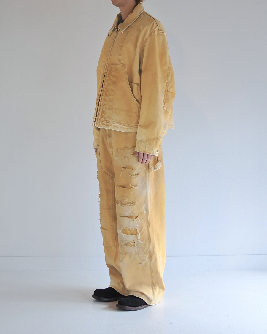 シルエットはゆとりのある身幅とややクロップド丈で設計しており、イエローカラーの鮮やかなトーンがレイヤードスタイルをより引き立てます。インナーアイテムとの重ね着がしやすいバランスに仕上げています。
生地には頒布の中で最も薄手の11号帆布を採用しており、強度・耐久性に優れるだけでなく、着用を重ねるごとにアタリなどの経年変化を楽しめる素材です。また、特殊エイジング加工を施すことで、水や薬品の使用量を抑えながら生地の凹凸が強調され、イエローの色味に自然なフェード感を加えています。