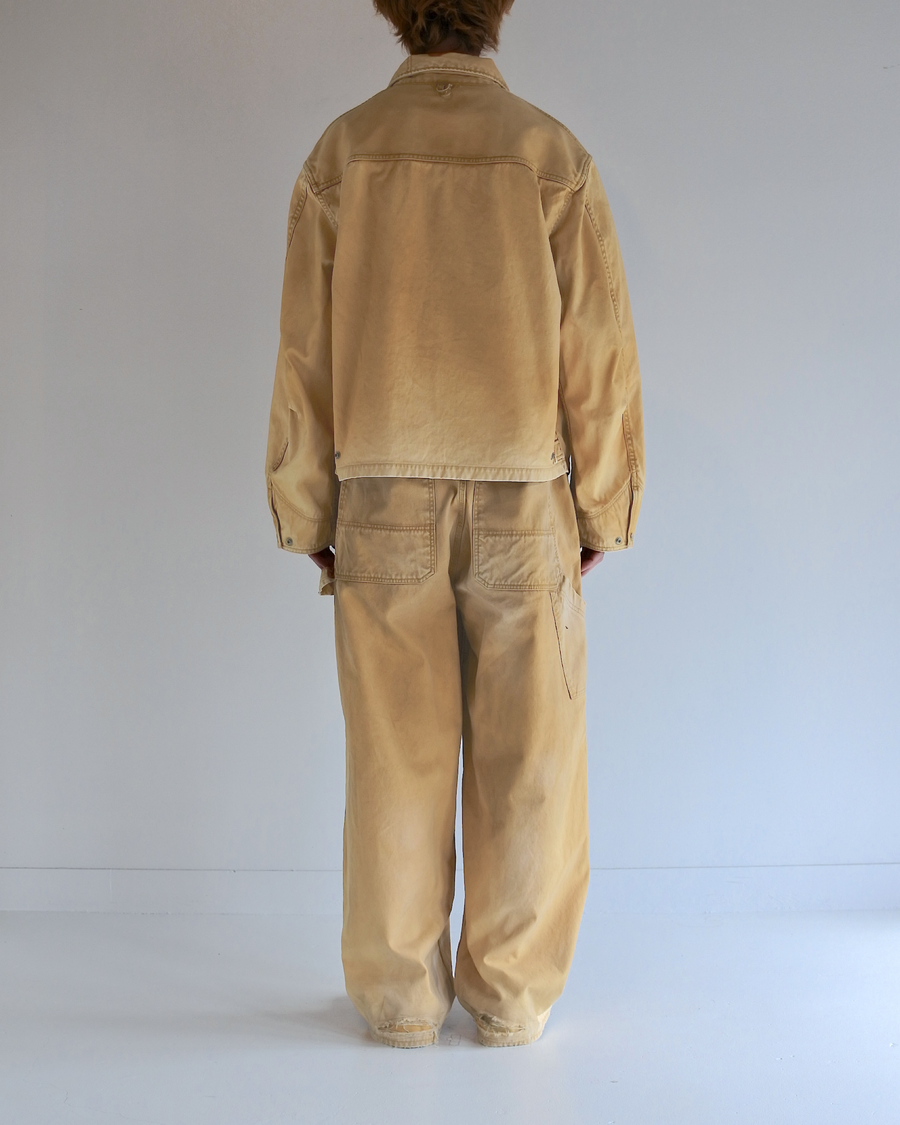 シルエットはゆとりのある身幅とややクロップド丈で設計しており、イエローカラーの鮮やかなトーンがレイヤードスタイルをより引き立てます。インナーアイテムとの重ね着がしやすいバランスに仕上げています。
生地には頒布の中で最も薄手の11号帆布を採用しており、強度・耐久性に優れるだけでなく、着用を重ねるごとにアタリなどの経年変化を楽しめる素材です。また、特殊エイジング加工を施すことで、水や薬品の使用量を抑えながら生地の凹凸が強調され、イエローの色味に自然なフェード感を加えています。