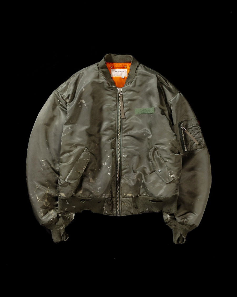 忠実なディテールを保ちながら、シルエットを現代的に整えたMA-1ジャケット。加工によりヴィンテージの風合いを再現した一着です。肉厚でミリタリーらしいツイル生地を使用し、打ち込みの密度や肌触りまでビンテージMA-1に近い仕上がりに。さらに、ダートペイントや特殊吹き付け、ダメージ加工を重ね、洗いをかけて染料を自然に剥がすことで、深みのある表情を生み出しています。カラーはオリーブ。